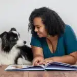 Frau liegt mit Border Collie auf dem Boden und liest ein Buch.